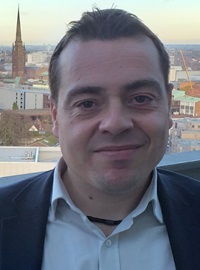 A photograph of David Hope, the HDRC's Coventry Coty Council Research Ambassador. David smiles at the camera and Coventry Cathedral is visible in the background.