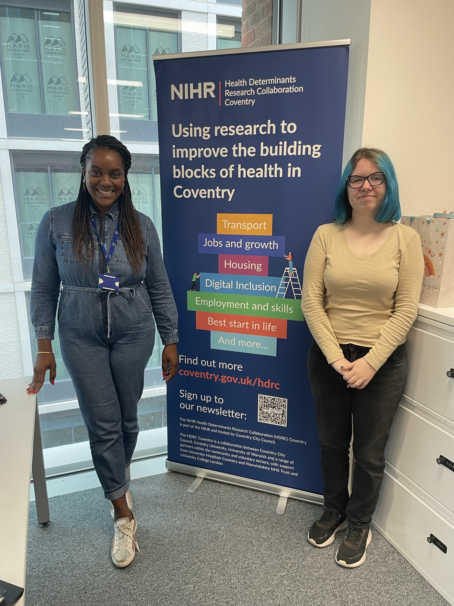 A photograph of Ida Slavina and Jessica Weeks in front of a HDRC banner.