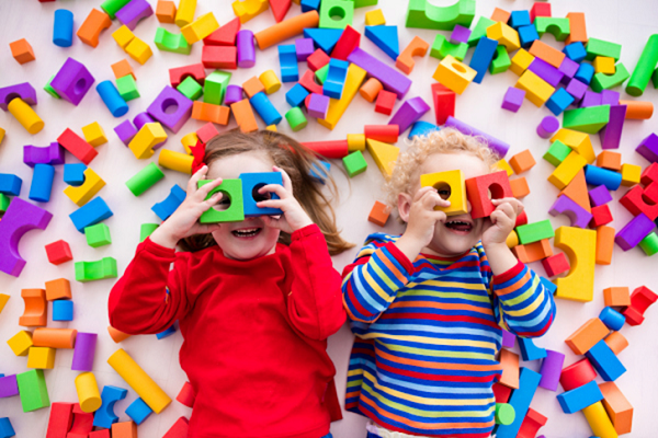 Two children lying on the floor, surrounded by colourful wooden blocks.